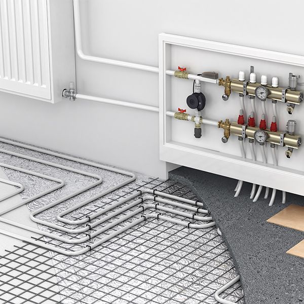 Underfloor heating system installation with tubing, manifold, and radiator pipes against a white wall.