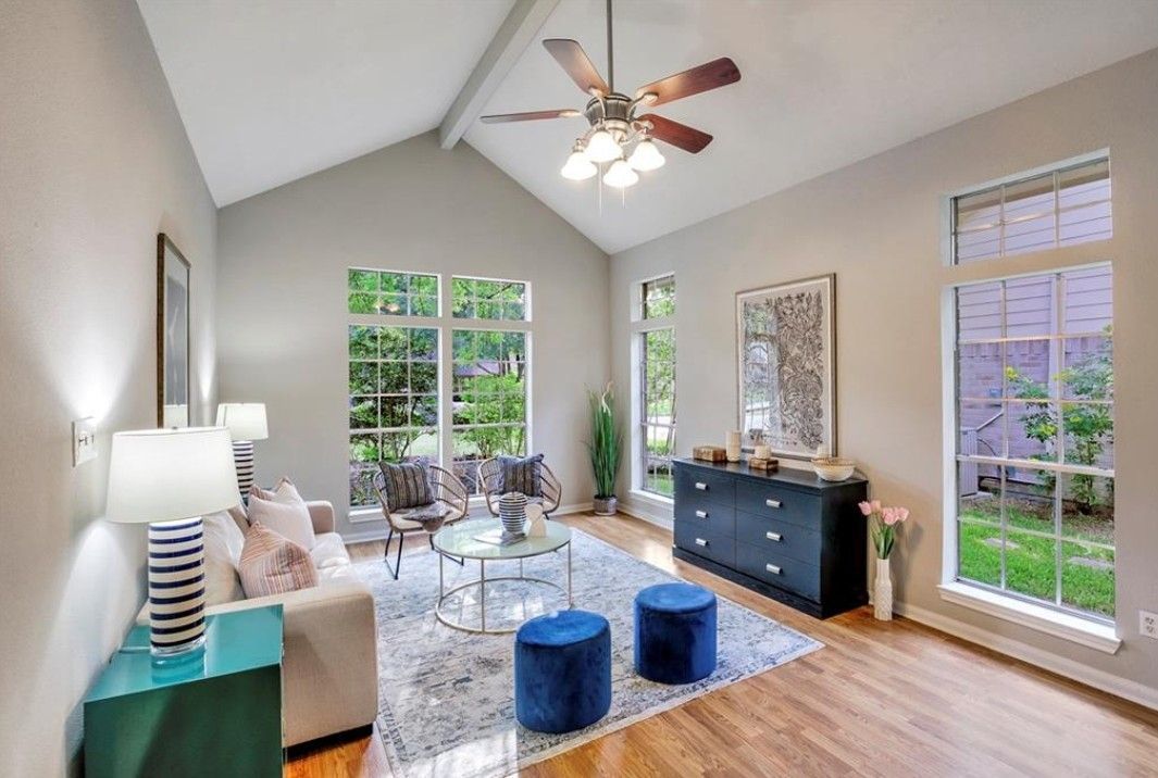 Living room with high ceiling, large windows, blue accents, and hardwood floors.