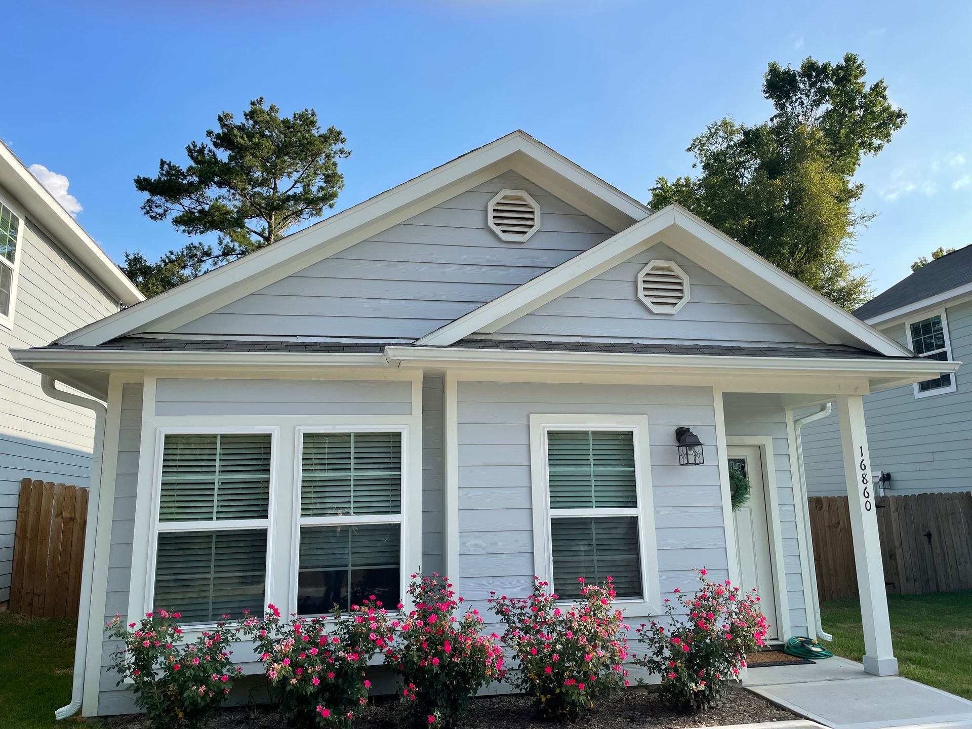Light blue house with white trim, two windows, and small red flowers in front.