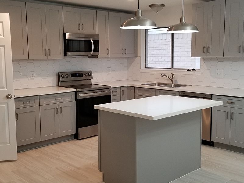 Gray kitchen with light-colored cabinets, stainless steel appliances, and a central island with a white countertop.