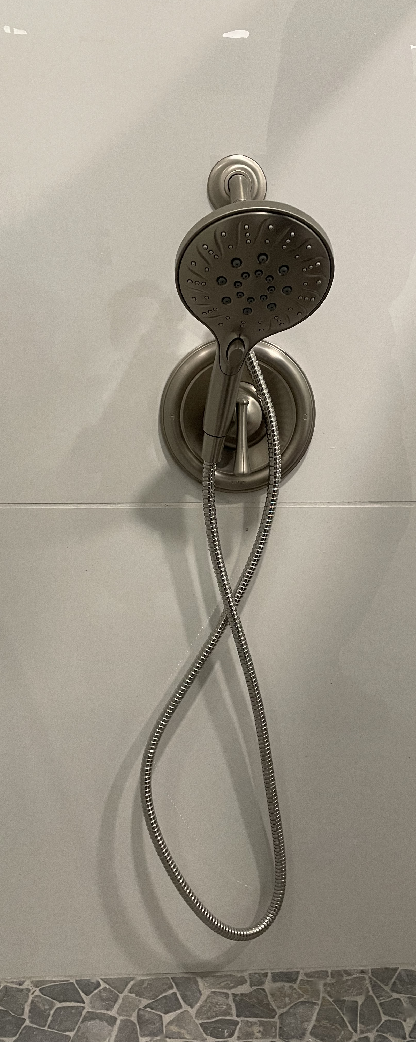 Showerhead with a flexible metal hose on a tiled wall.