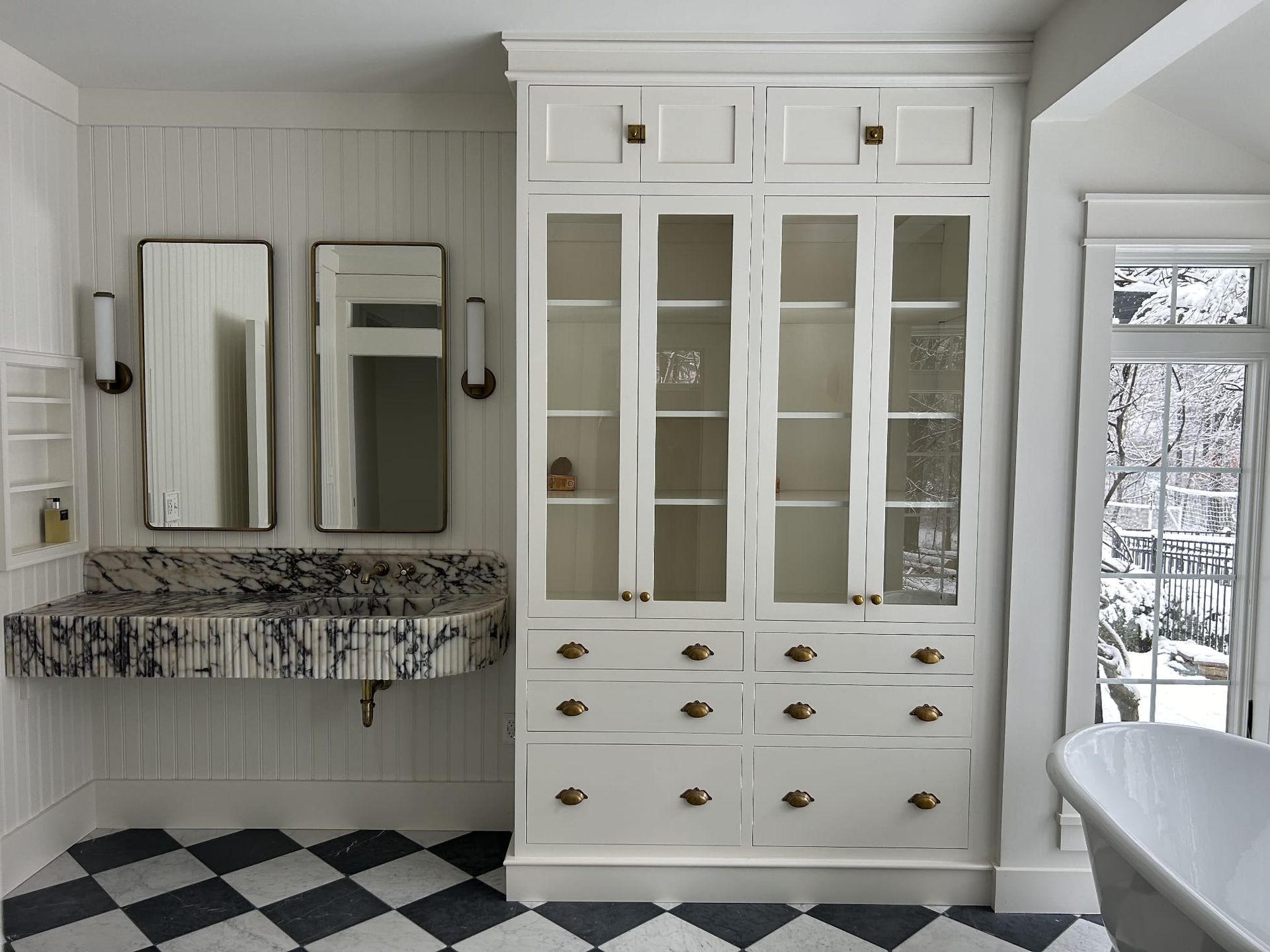 White bathroom with double mirrors, stone vanity, glass-front cabinet, and black-and-white checkered floor.