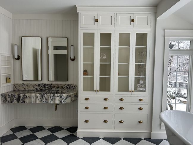 Bright bathroom with white vanity cabinet, mirrors, floral counter, and checkered black-and-white tile floor.