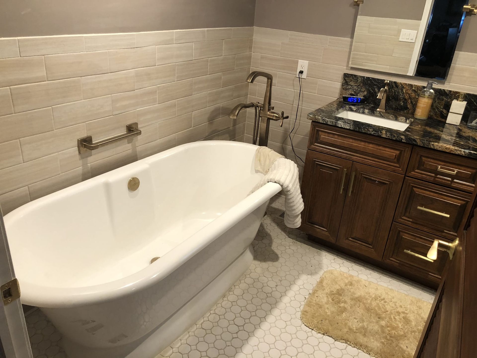 Bathroom with a white clawfoot tub, beige tile walls, and dark wood vanity next to a tan rug.