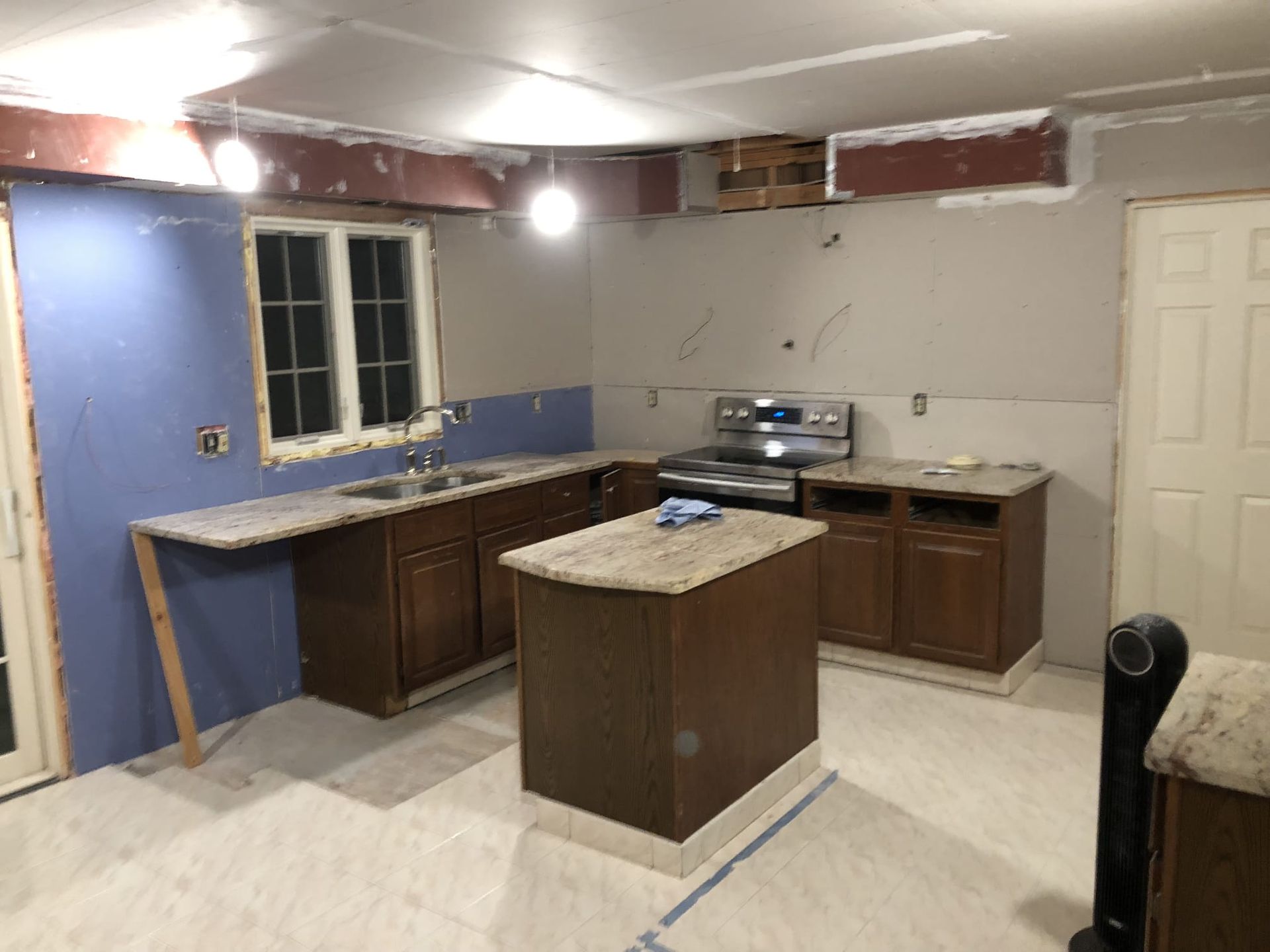 Partially renovated kitchen with cabinets, island, stove, window, and unfinished walls