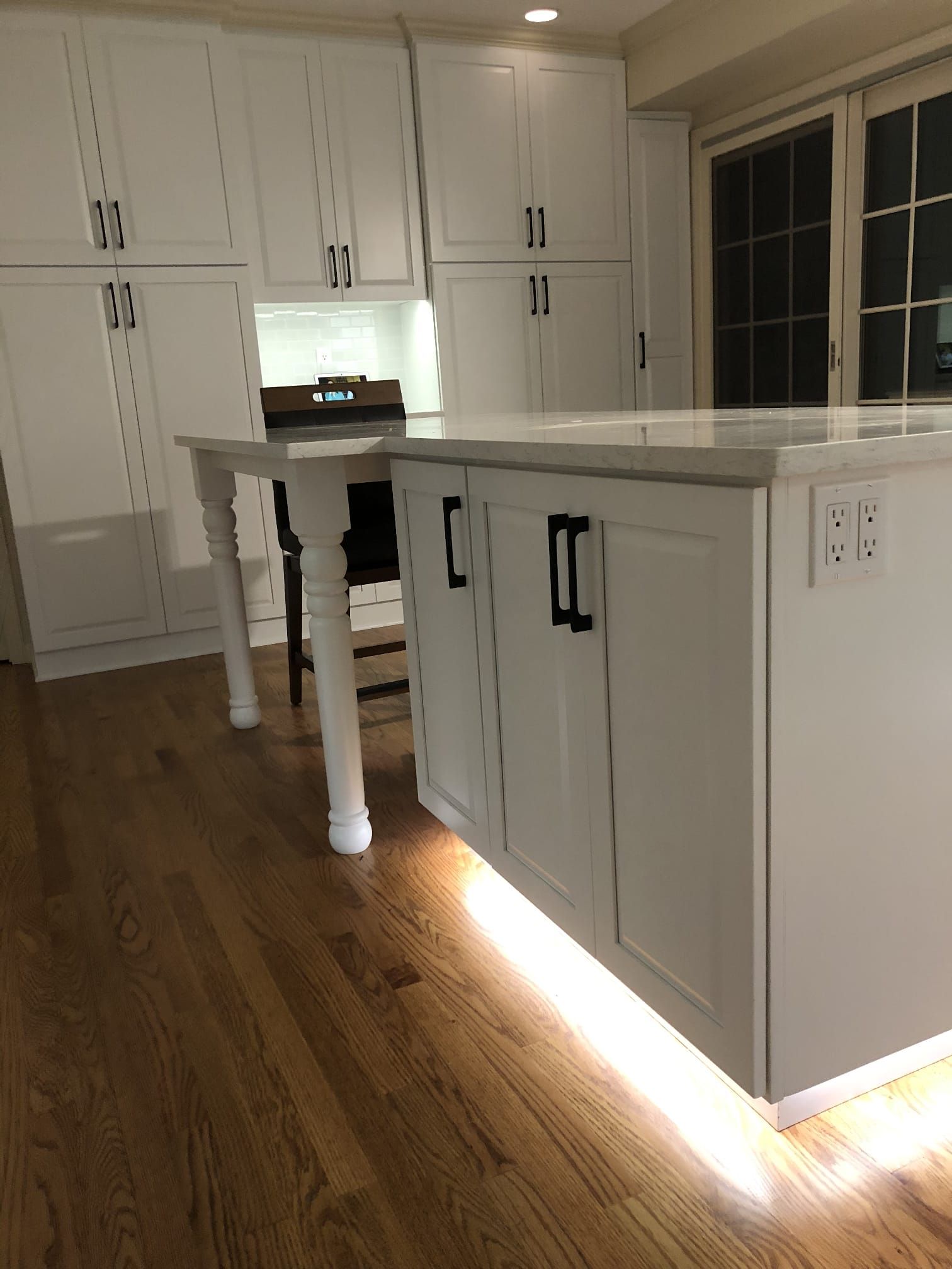 Modern white kitchen with island, black handles, wood floor, and under-cabinet lighting