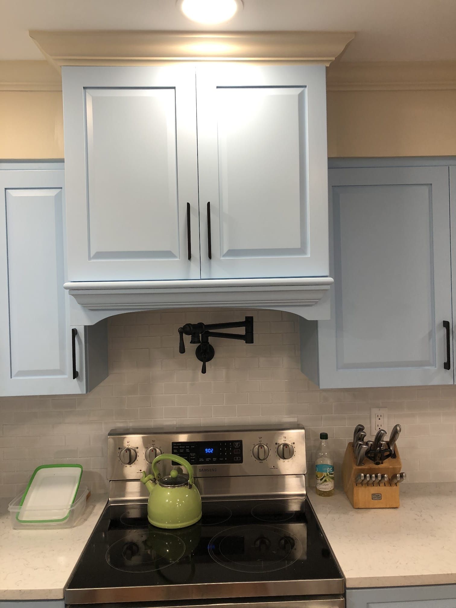 White kitchen cabinets above stainless stove with green kettle, under-cabinet light, and knife block on counter