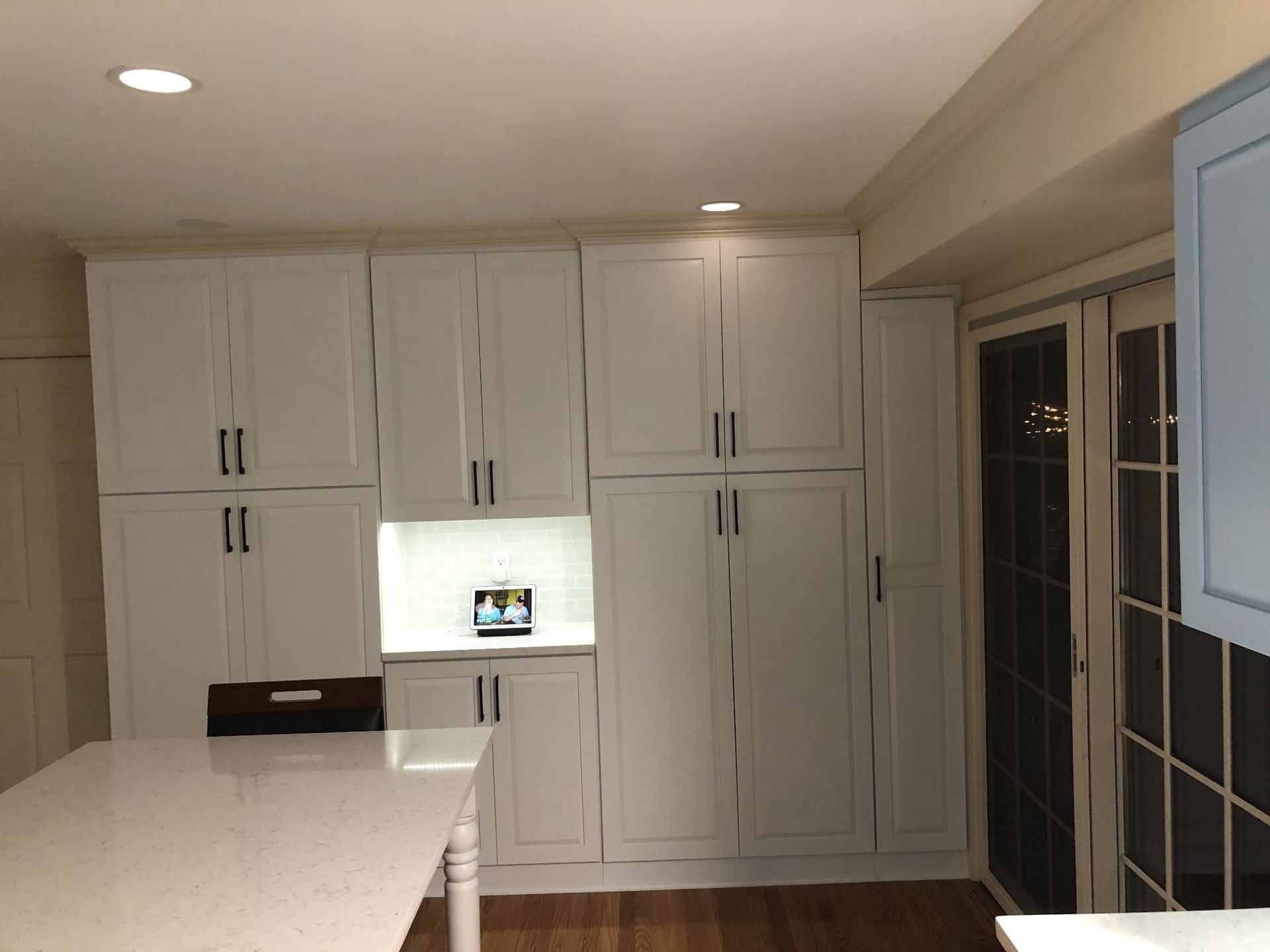 Bright white kitchen with large cabinets, island counter, and a small lit display inset in the wall.