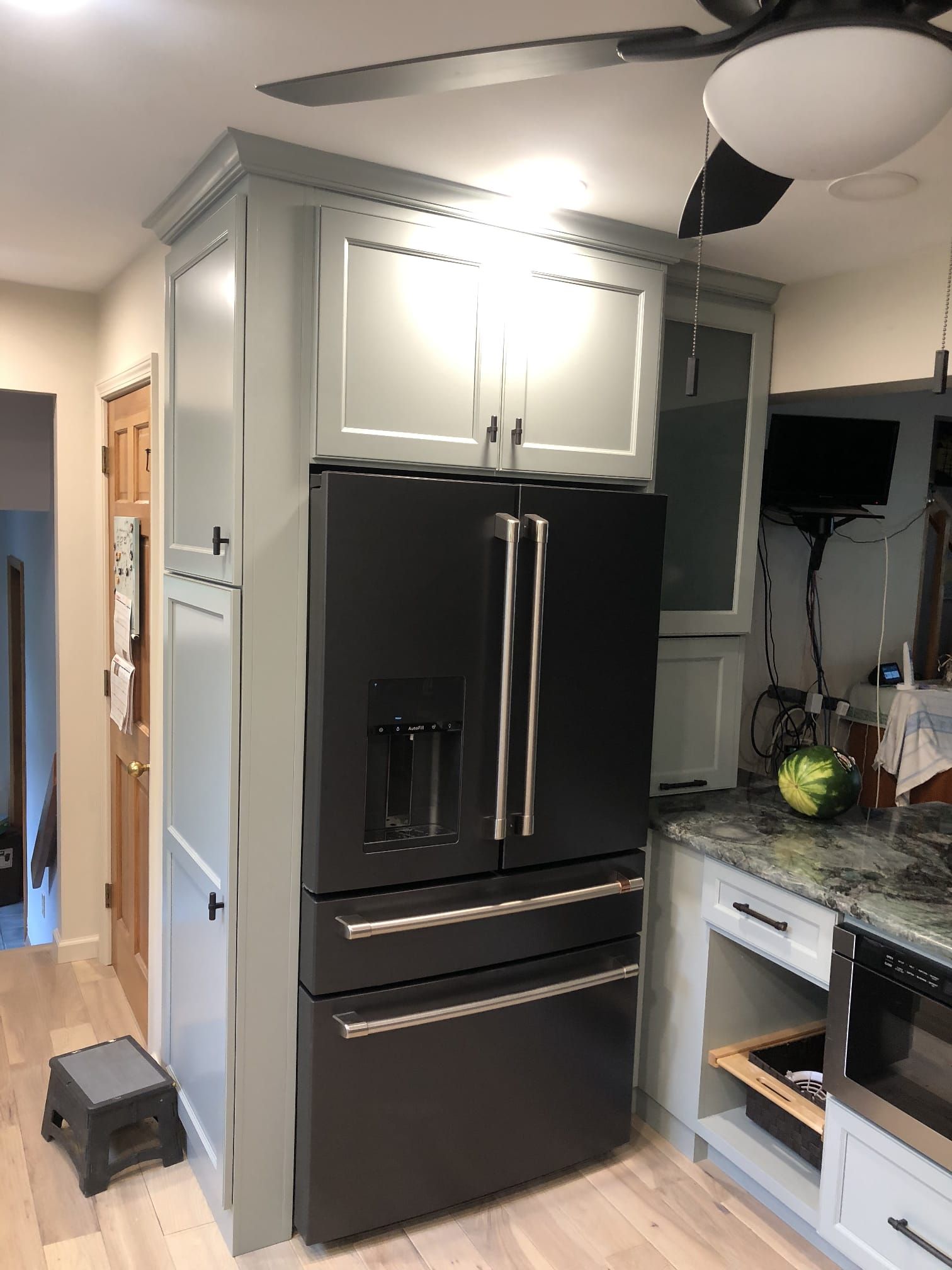 Black stainless French-door refrigerator in a modern kitchen with white cabinets and a ceiling fan