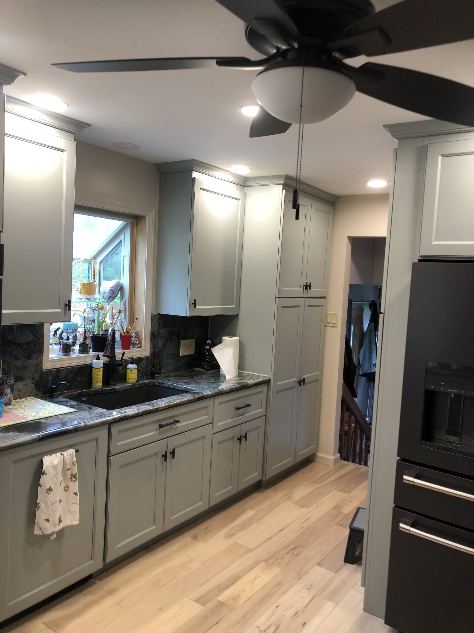 Modern kitchen with gray cabinets, black granite counters, light wood floor, and a ceiling fan.