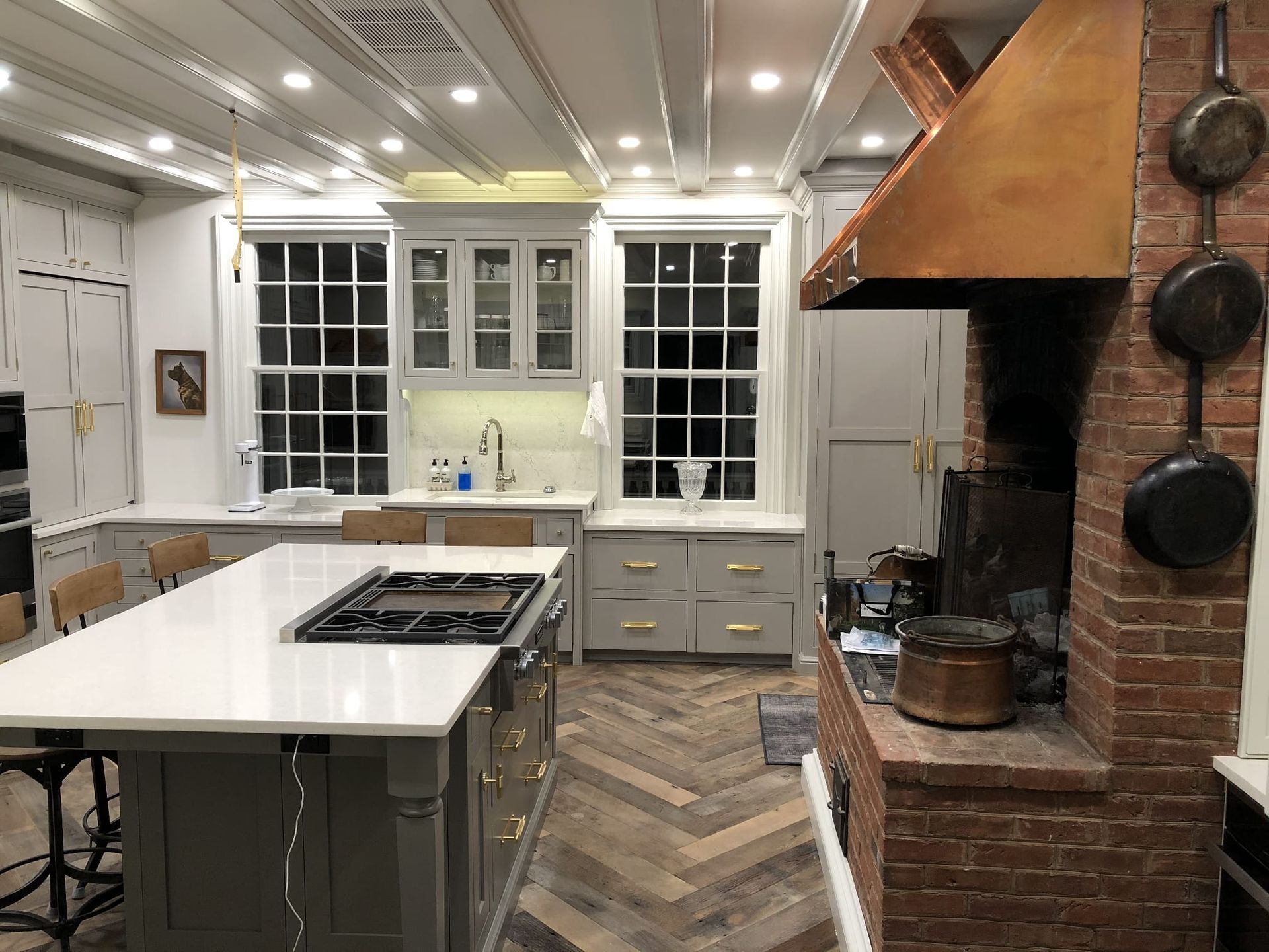 Bright white kitchen with island, herringbone wood floor, and brick fireplace mantel.