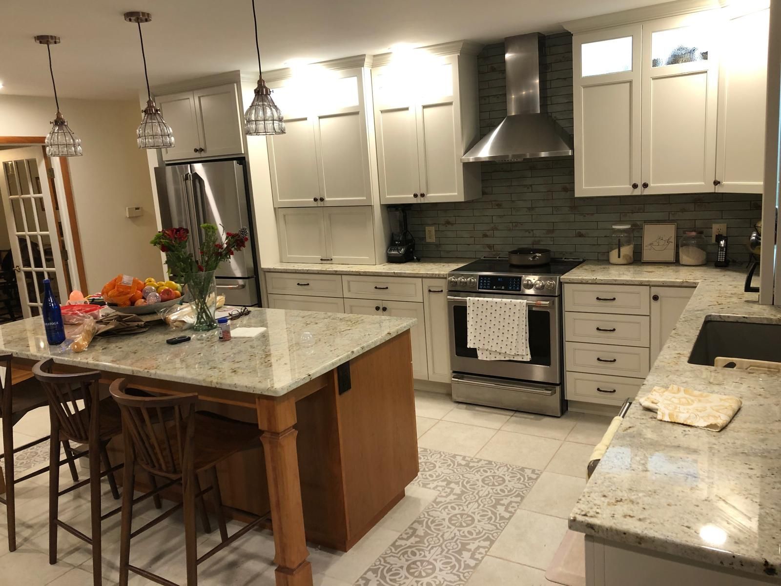 Bright kitchen with white cabinets, granite island, stainless stove, and tiled floor