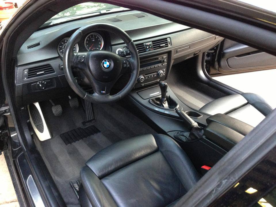 Black BMW interior with leather seats, dashboard, steering wheel, and center console visible from the open door