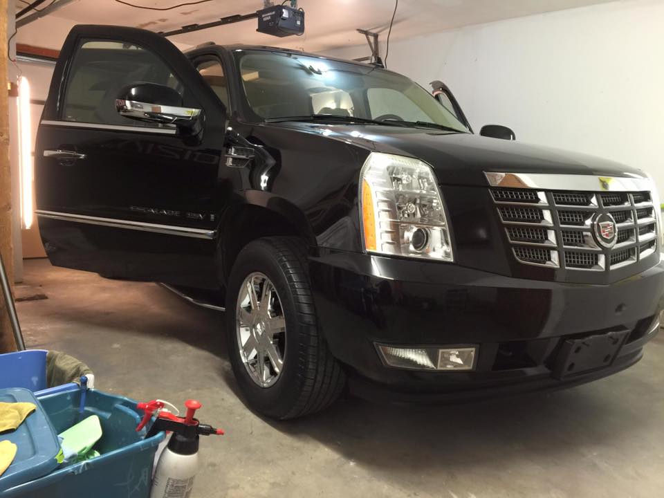 Black Cadillac SUV parked in a garage with the driver's door open.