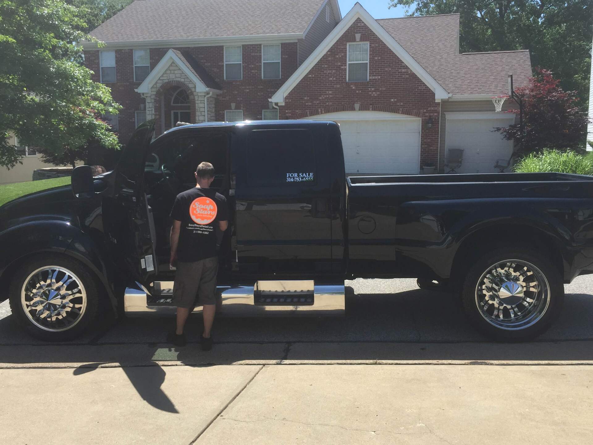 Black pickup truck parked on a driveway with a person standing beside it in front of a brick house.