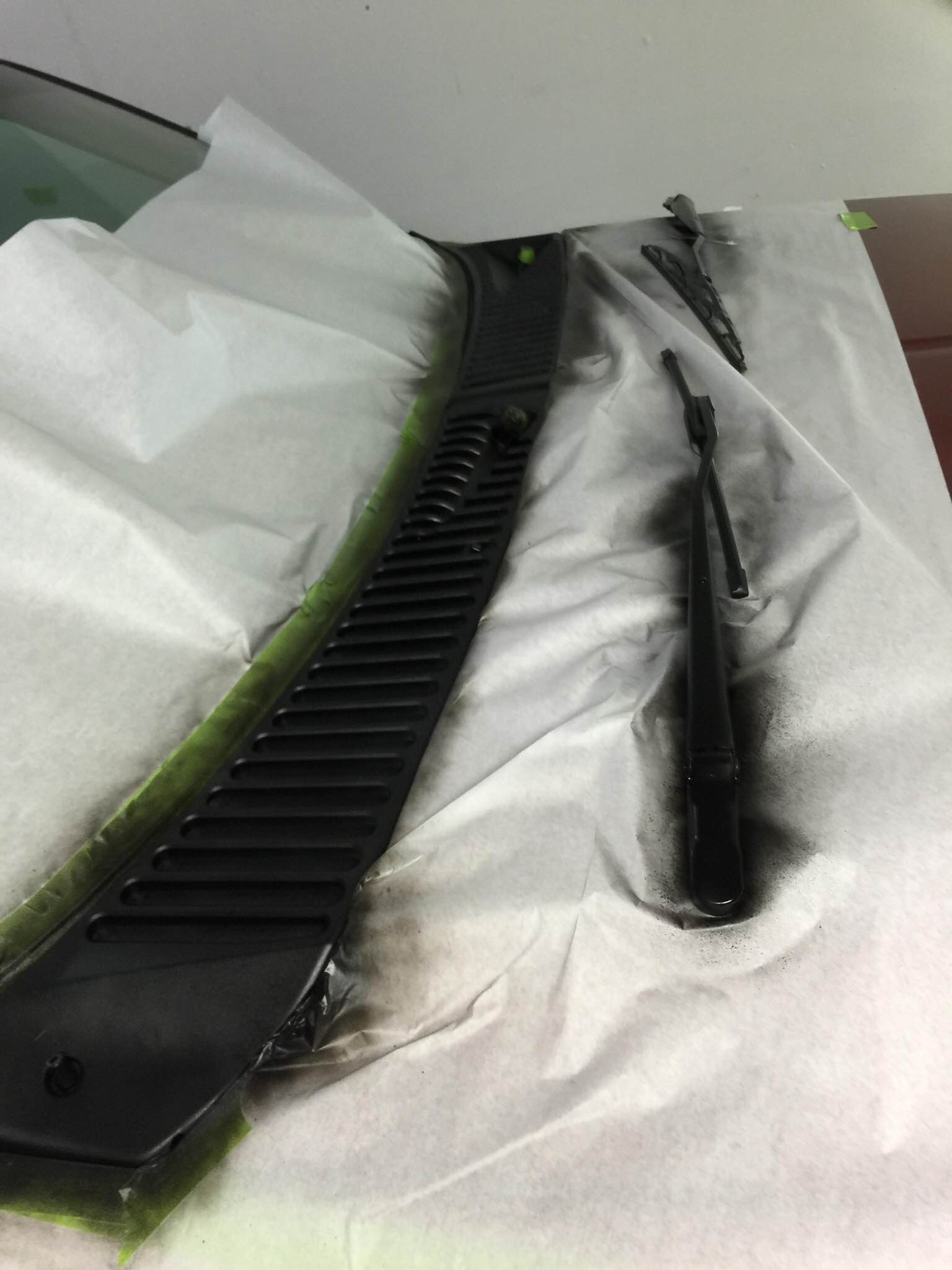 Black plastic car bumper parts laid on a white cloth, one curved and one narrow strip, with paint residue.