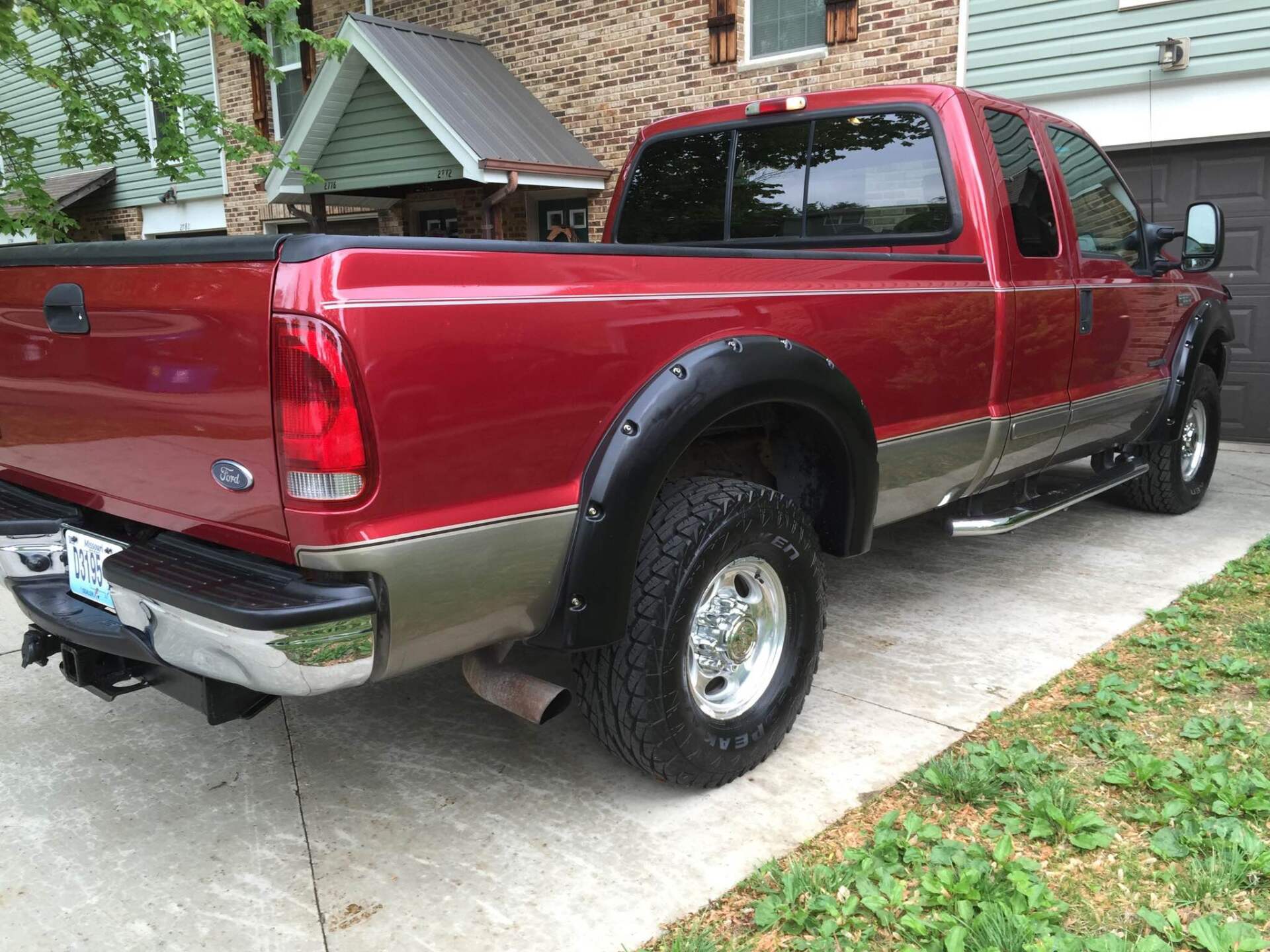 Red pickup truck parked in a driveway beside a house, viewed from the rear side.