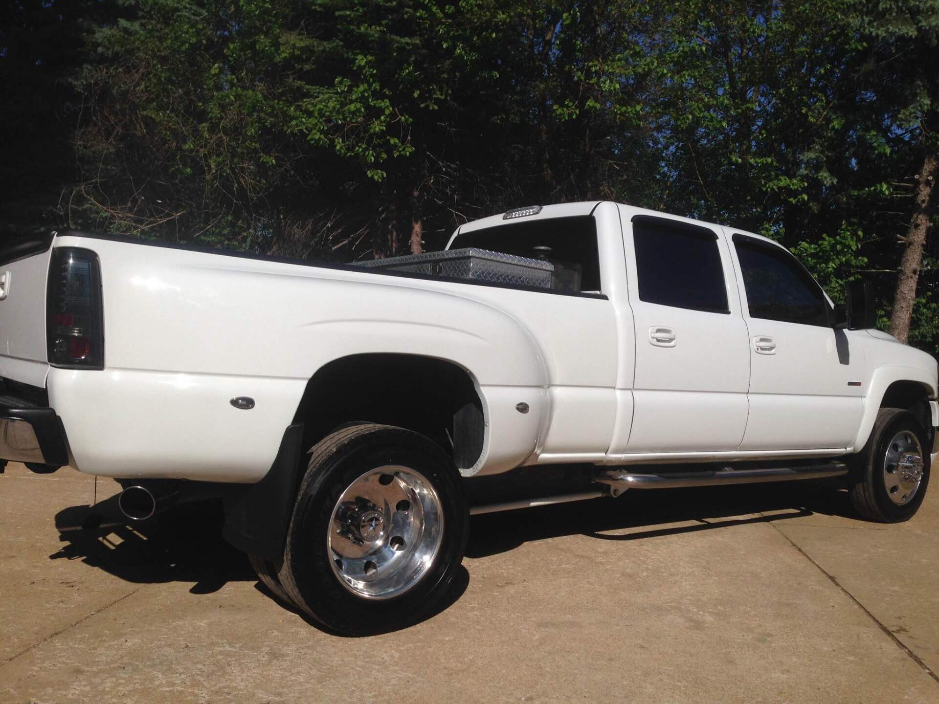 White lifted pickup truck parked outdoors on a driveway, side view