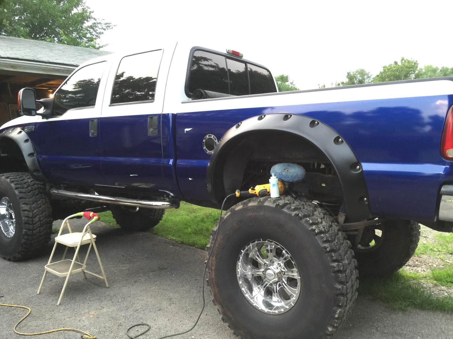 Lifted blue pickup truck with oversized tires parked outdoors on a driveway