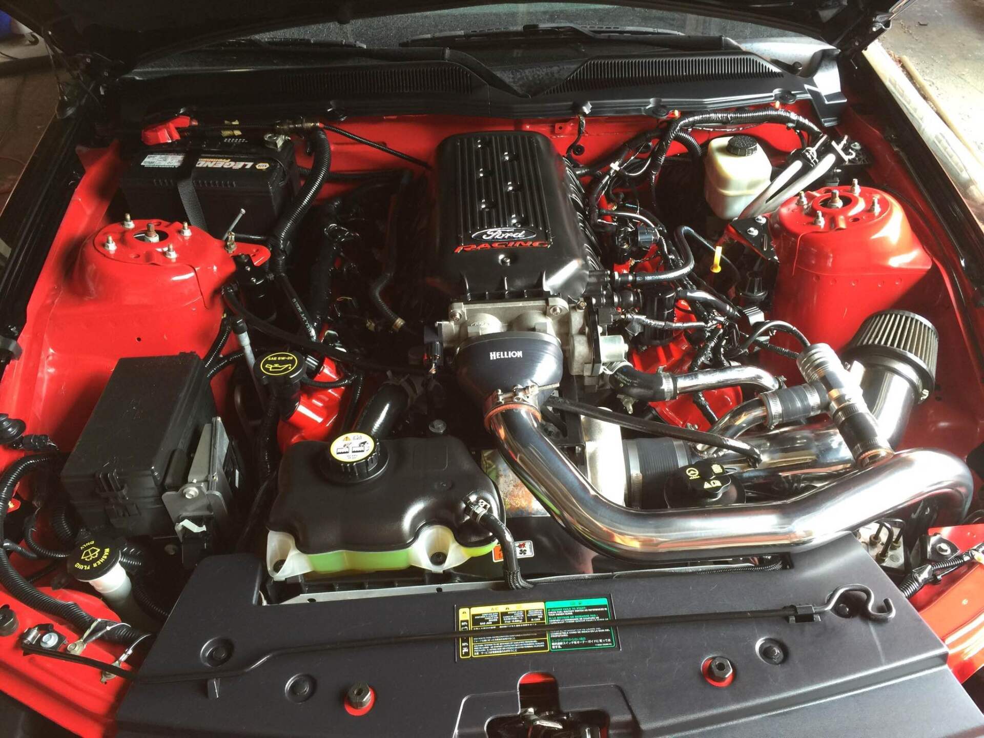 Open car engine bay with red strut towers and polished chrome intake piping