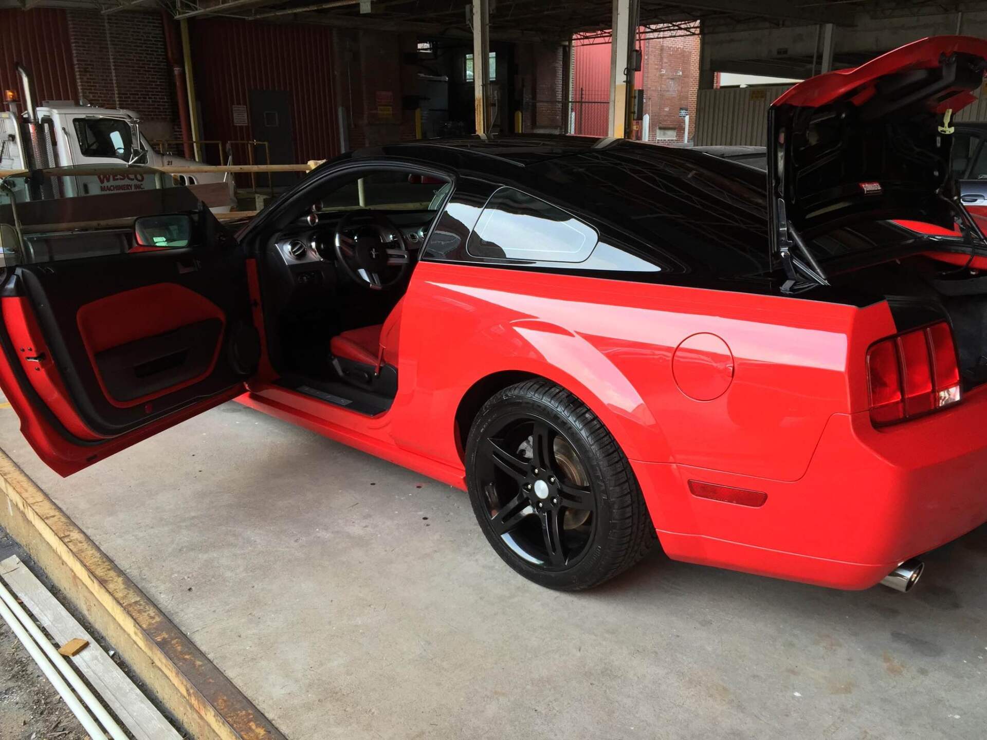 Red sports car with black racing stripes in a garage, driver door open and trunk open
