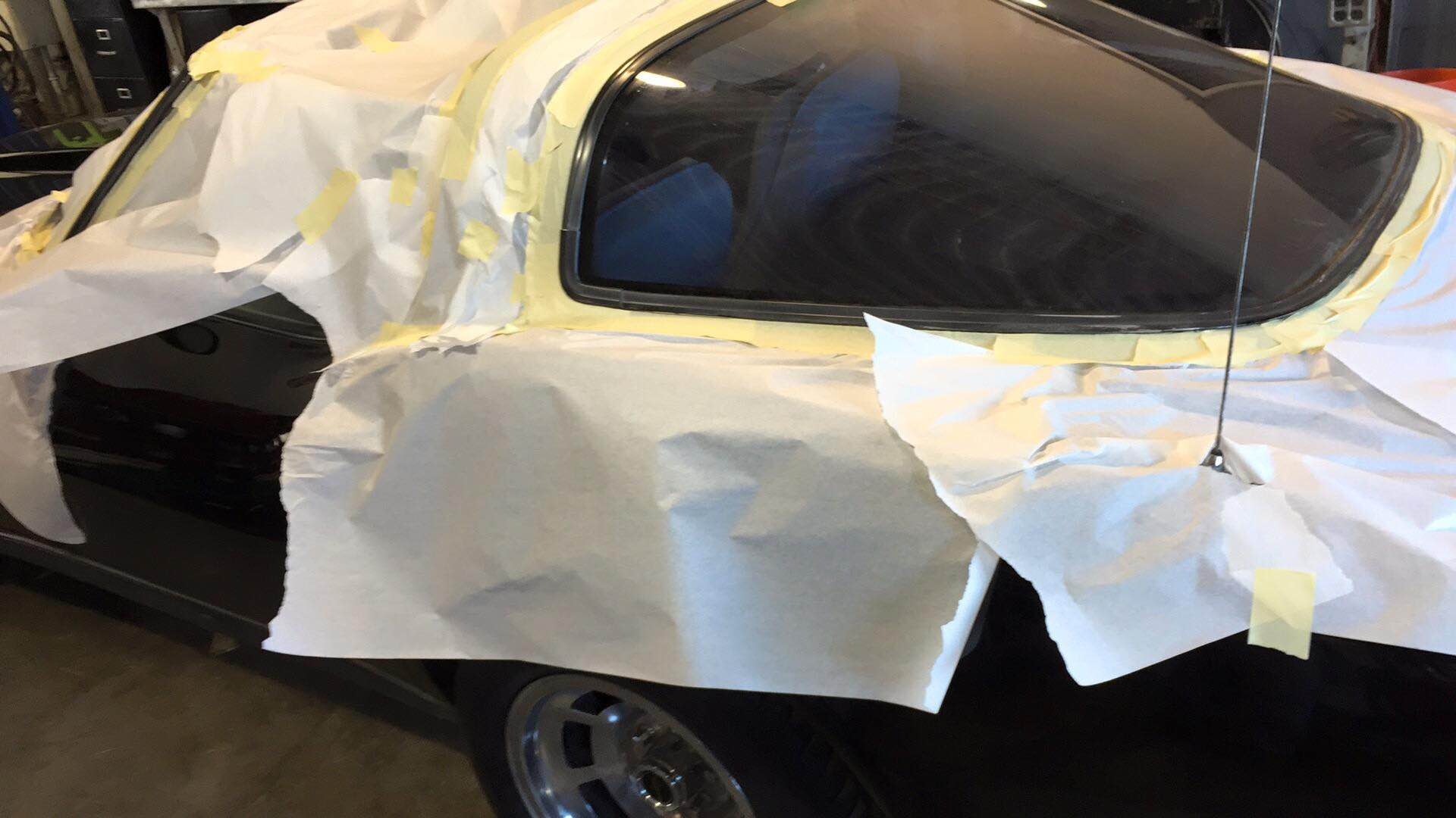 Car wrapped in white protective covering with taped seams, parked outdoors in a garage or driveway.