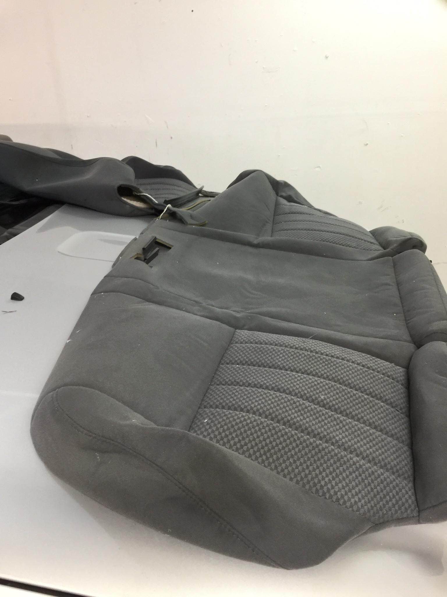 Gray textured handbag on a white surface, with a black strap in the background.
