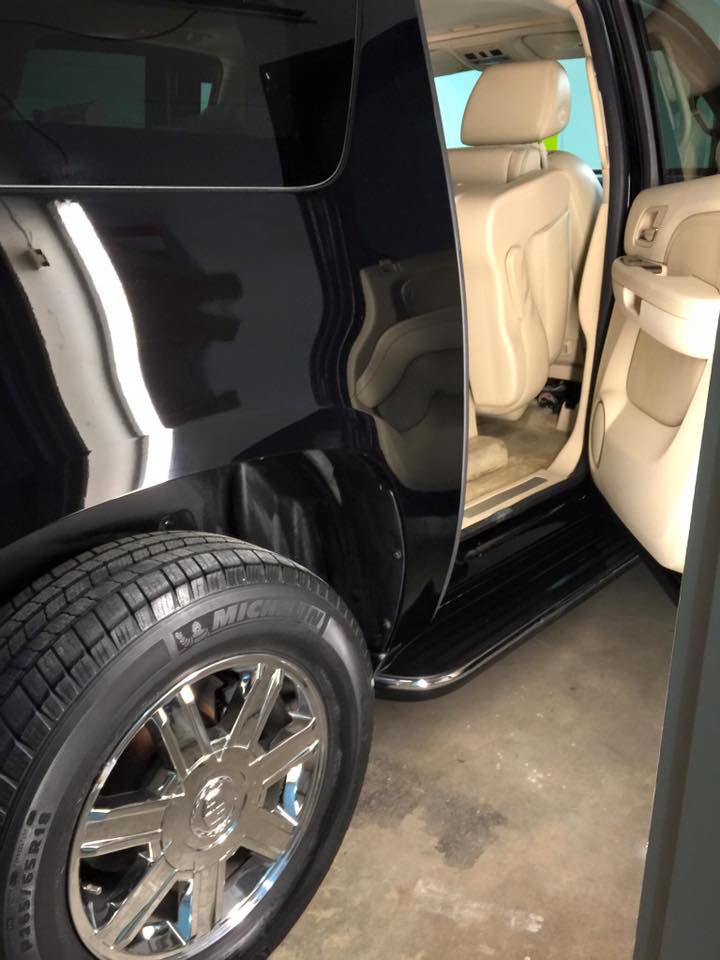 Black SUV with open rear door, beige leather interior, and chrome wheel in a garage.