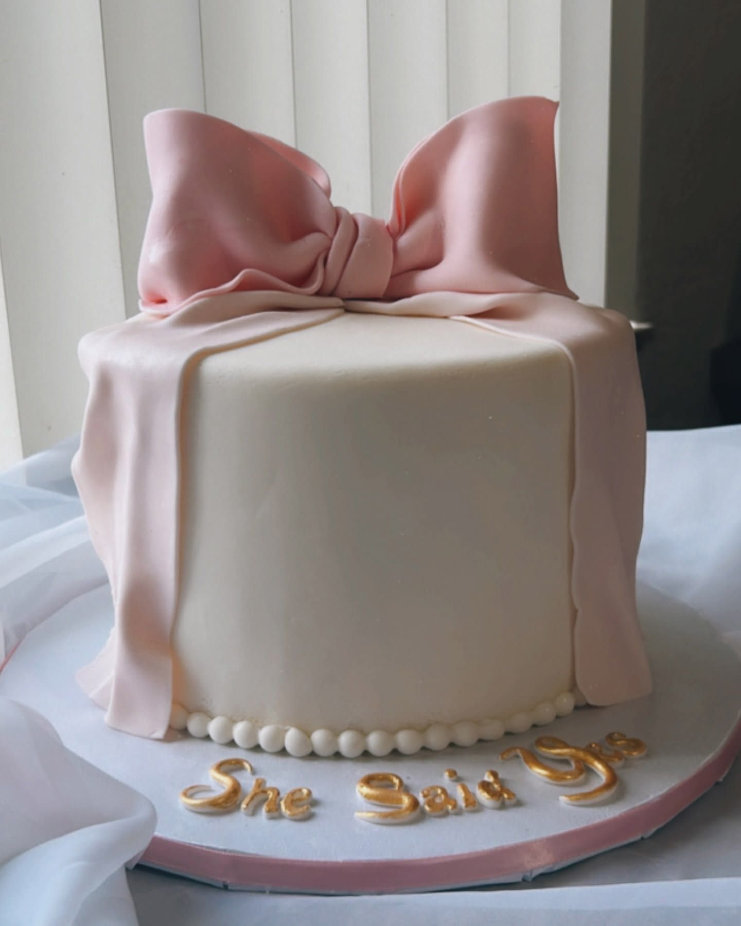 A white cake with a pink bow and the name she says on it