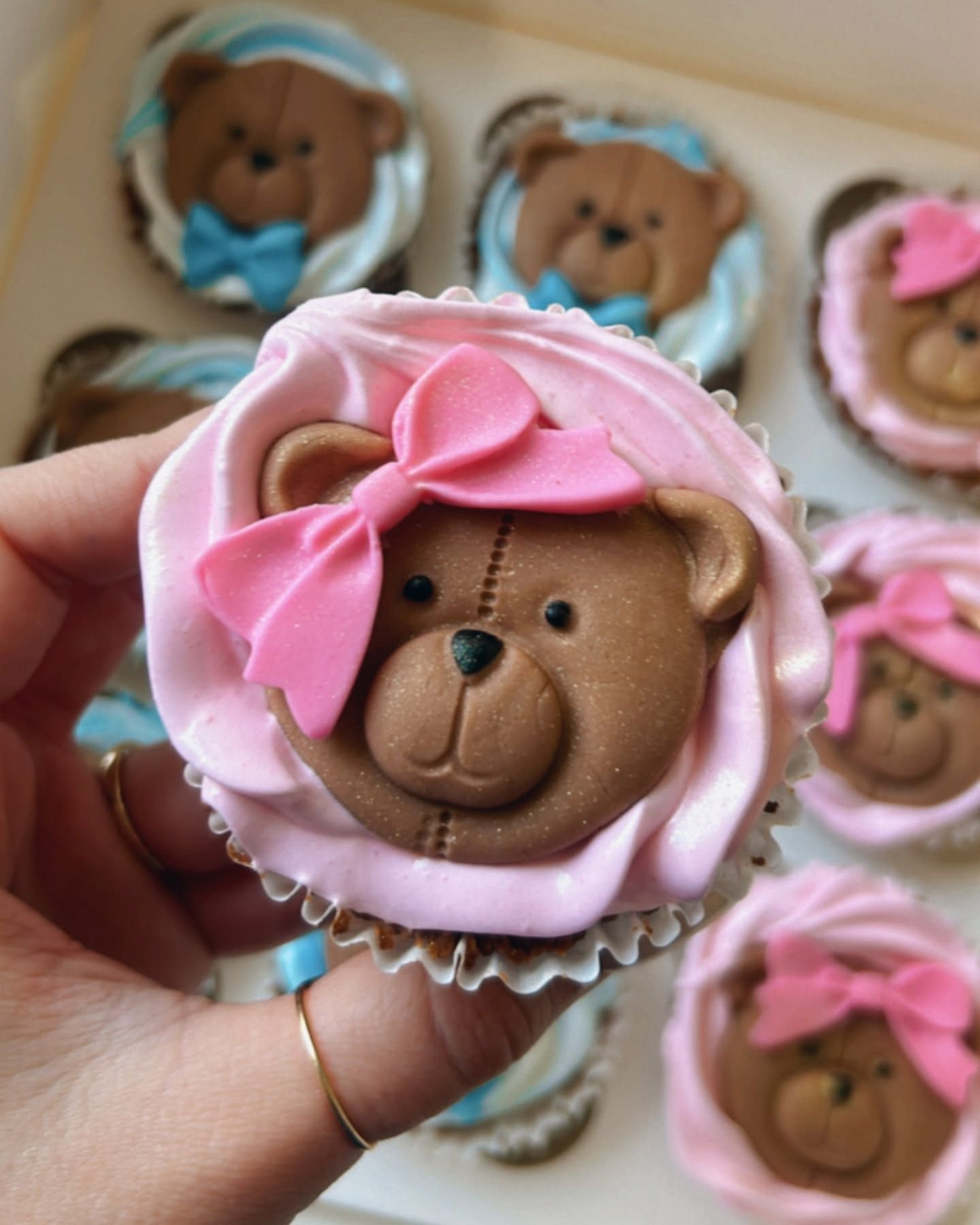 A person is holding a teddy bear cupcake with a pink bow