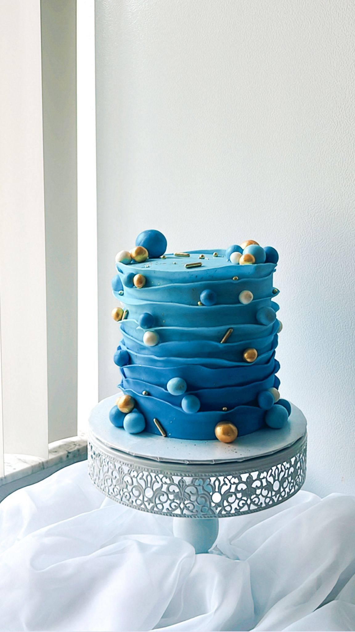 A blue cake is sitting on top of a silver cake stand on a table.