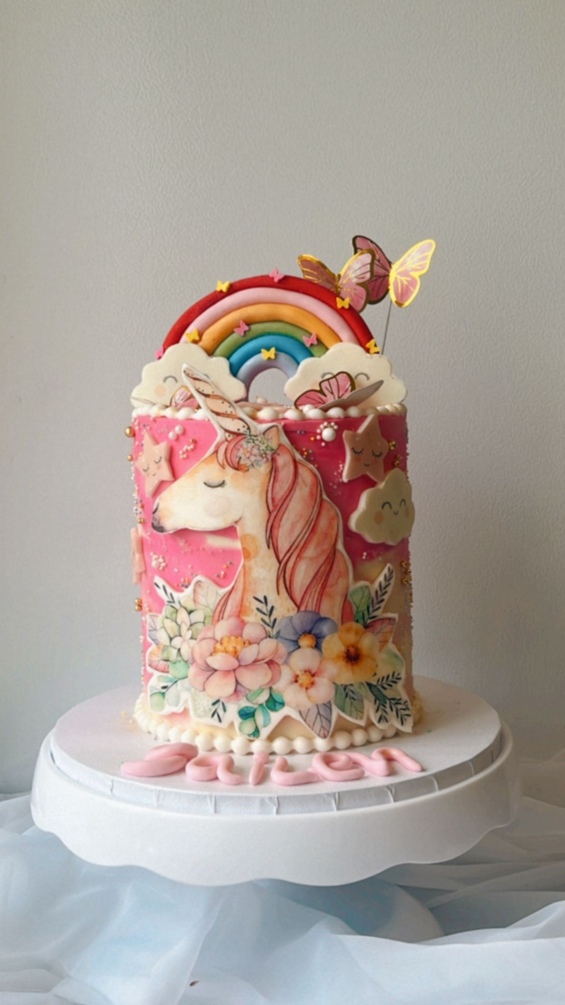 A cake with a unicorn and a rainbow on it is on a cake stand.