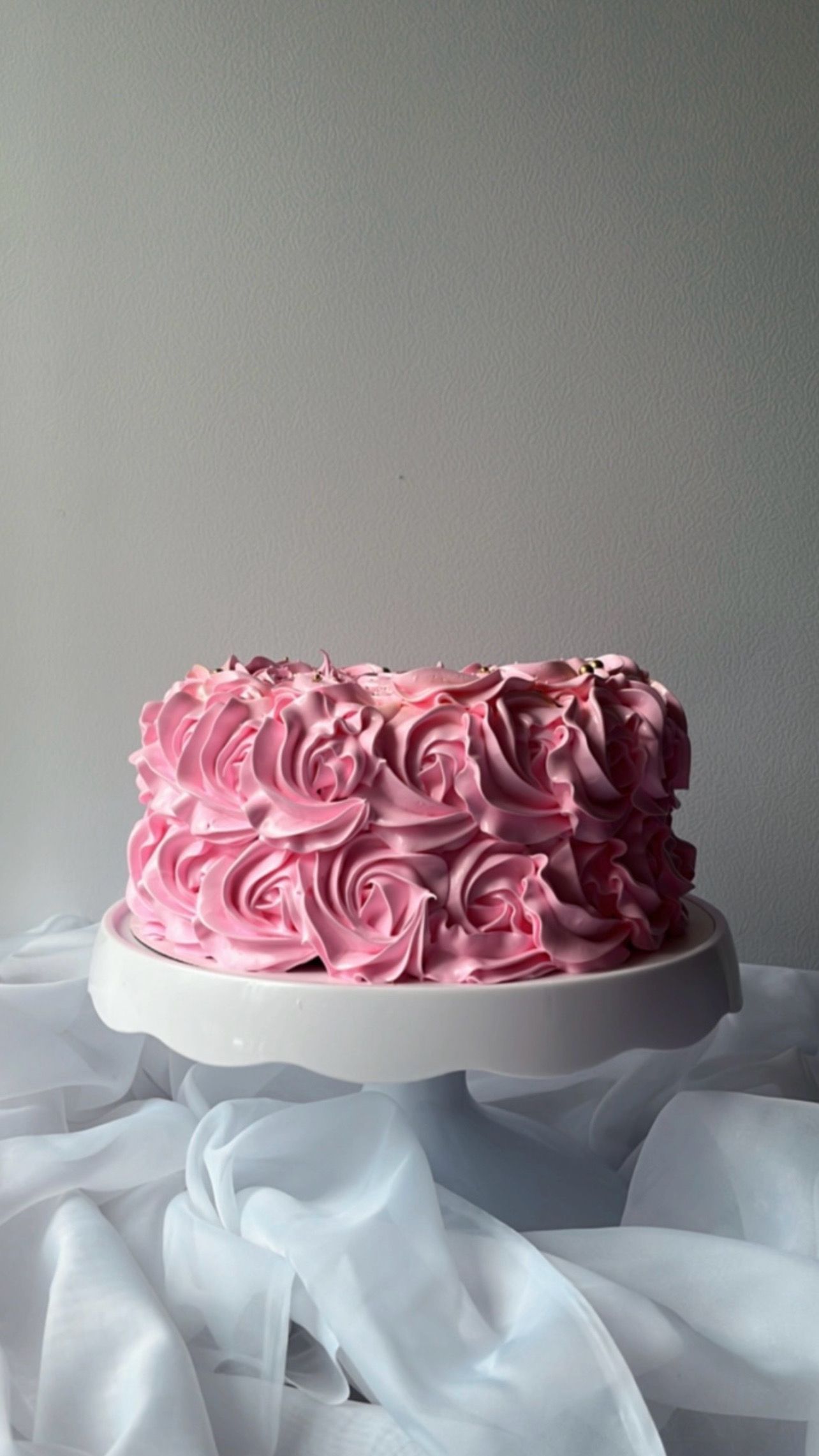 A cake with pink frosting is sitting on top of a white cake stand.