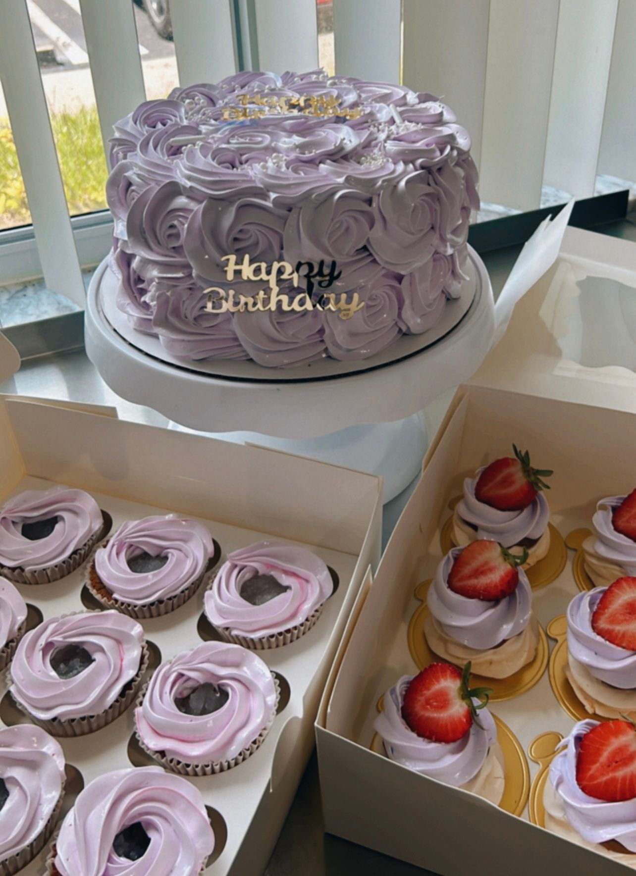 A birthday cake and cupcakes are sitting on a table.