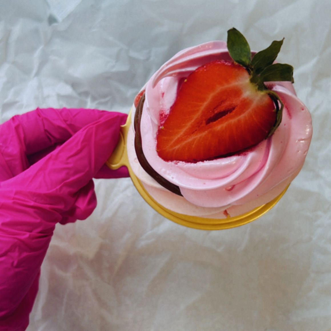 A person wearing pink gloves is holding a cupcake with a strawberry on top