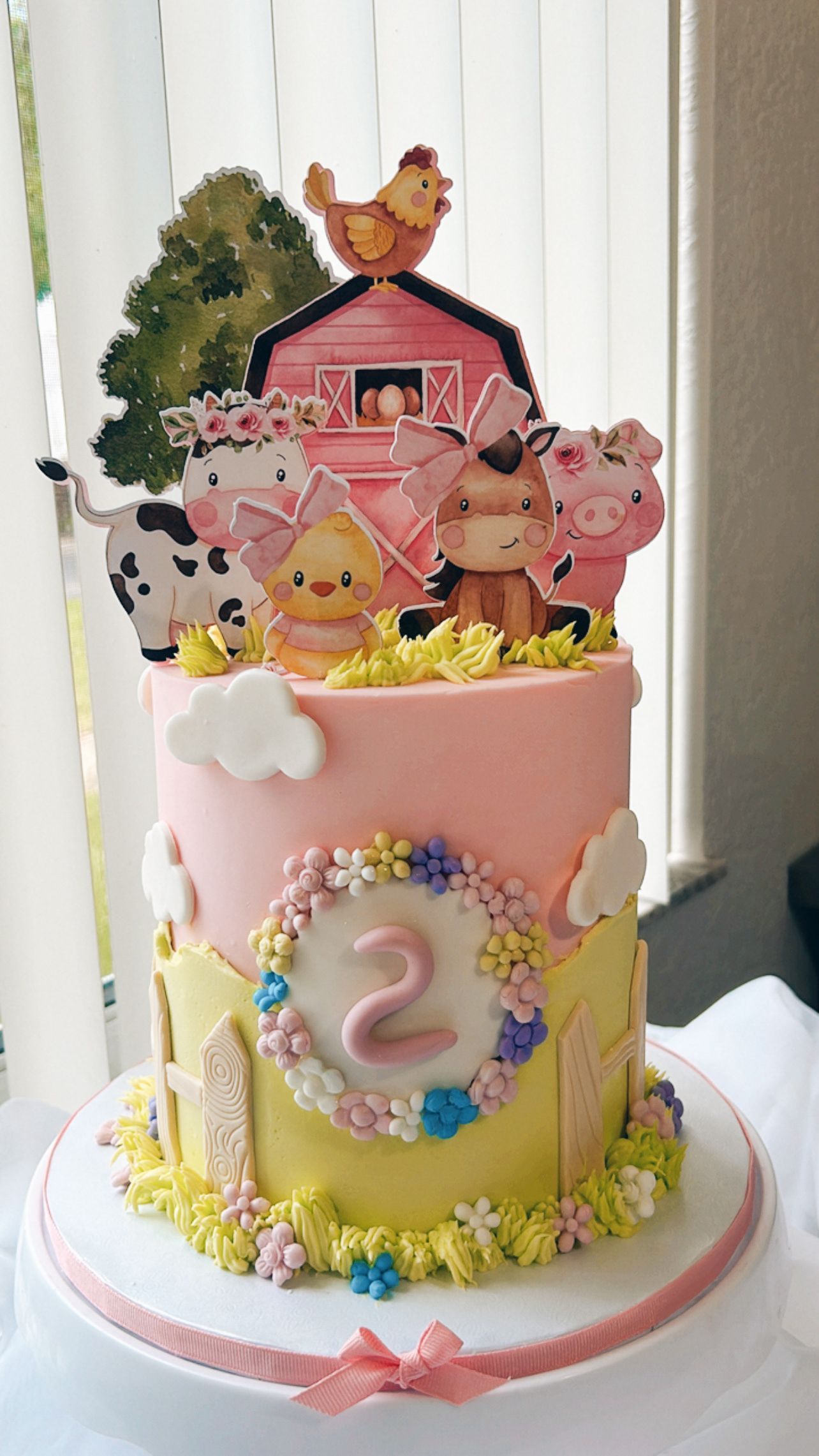 A pink and yellow cake with farm animals on top of it.