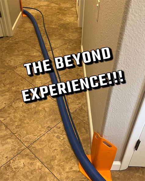Blue vacuum hose on tan tile floor near wall, with orange cleaner, captioned “THE BEYOND EXPERIENCE!!!”
