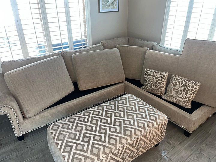 Beige sectional sofa with patterned ottoman in a bright living room by windows
