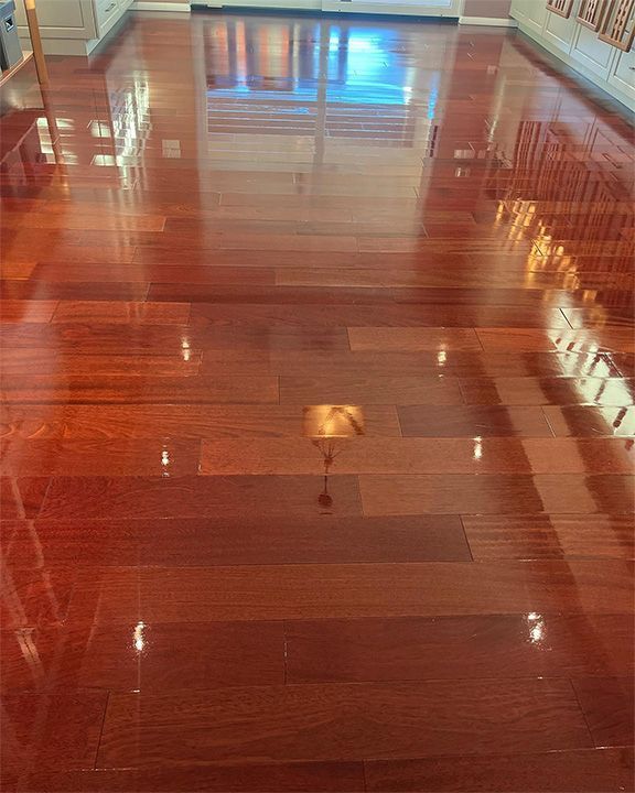 Shiny hardwood floor reflecting ceiling lights in an empty room with a polished wooden finish