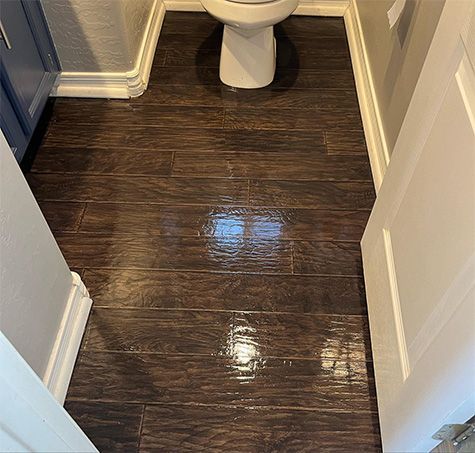 Small bathroom with dark wood-look floor, white toilet, and open doorways on both sides