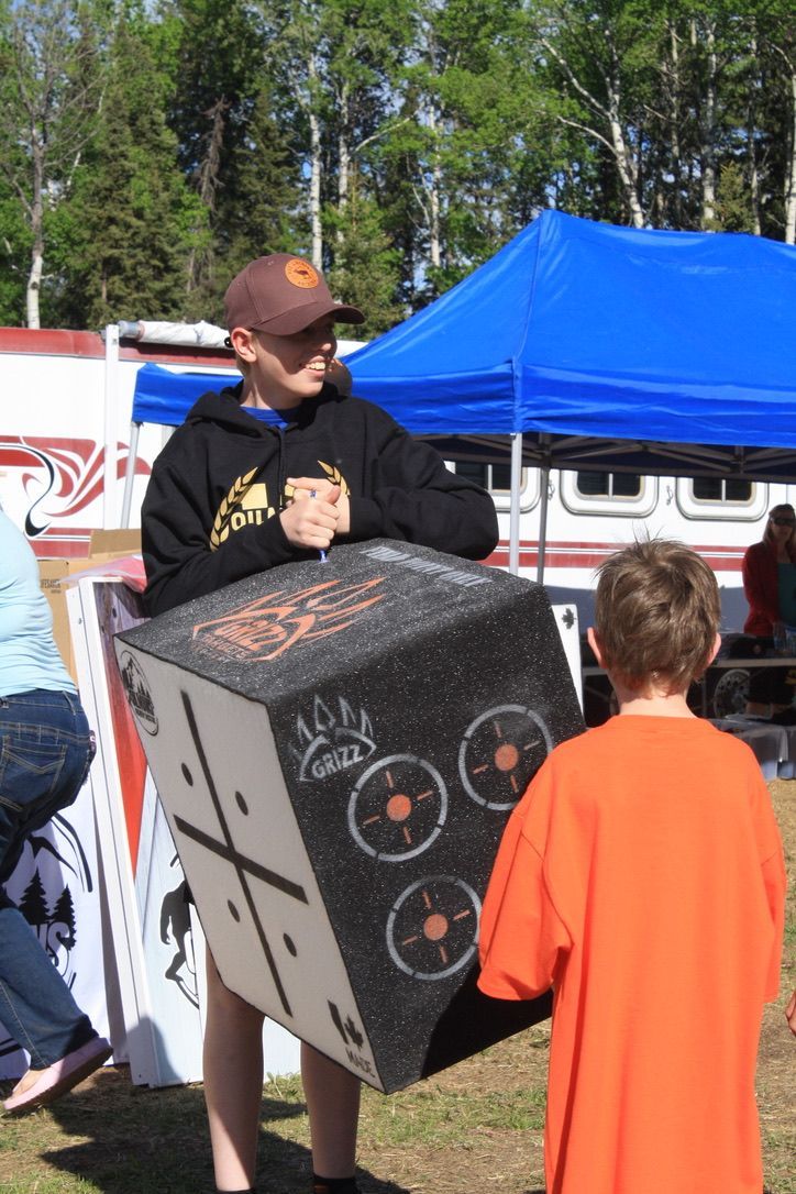 A boy in an orange shirt is standing next to a man carrying a large box