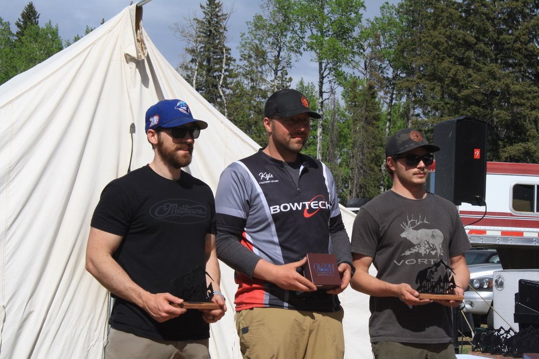 Three men standing in front of a tent holding trophies