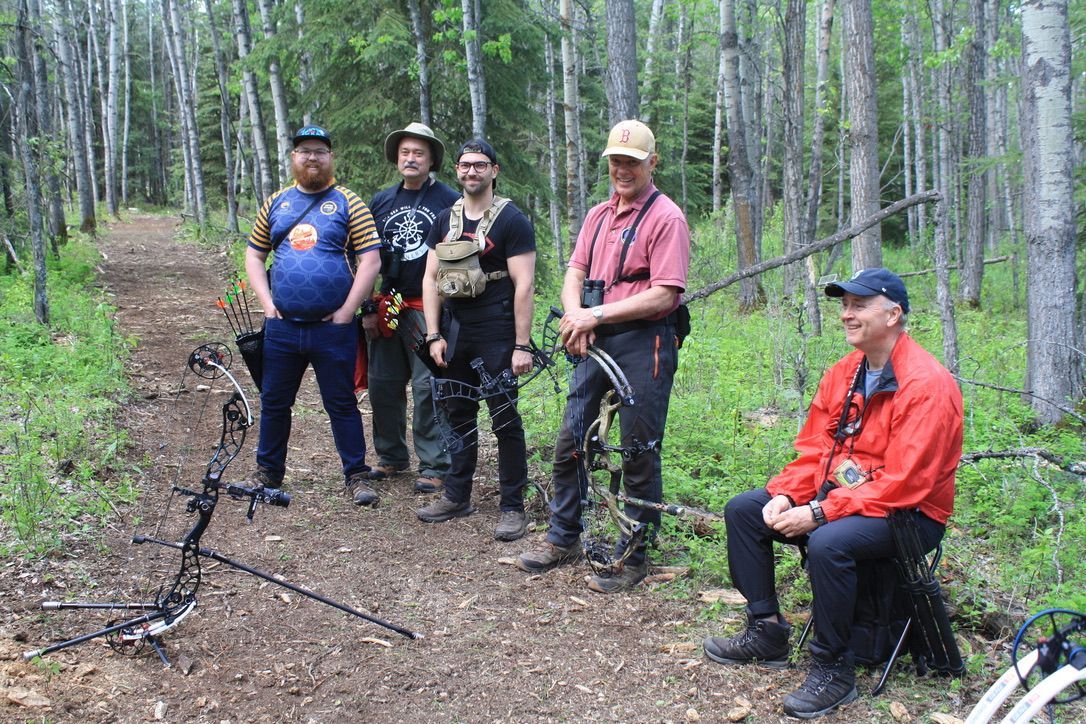 A group of men are standing in the woods holding bows and arrows.