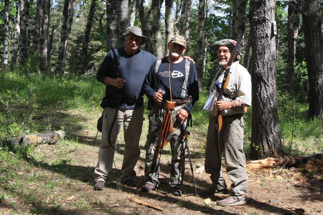 Three men are posing for a picture in the woods