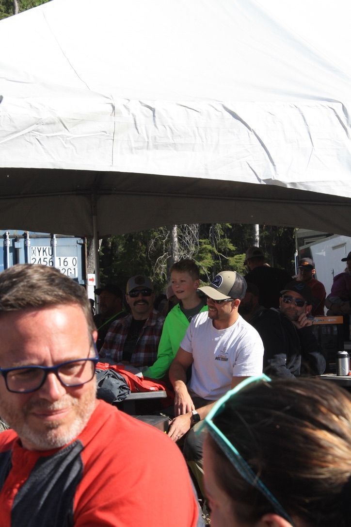 A group of people sitting under a tent including a man wearing glasses