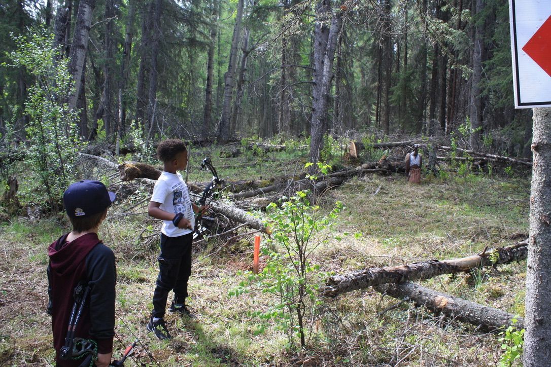 Two young boys are standing in the woods holding bows and arrows.