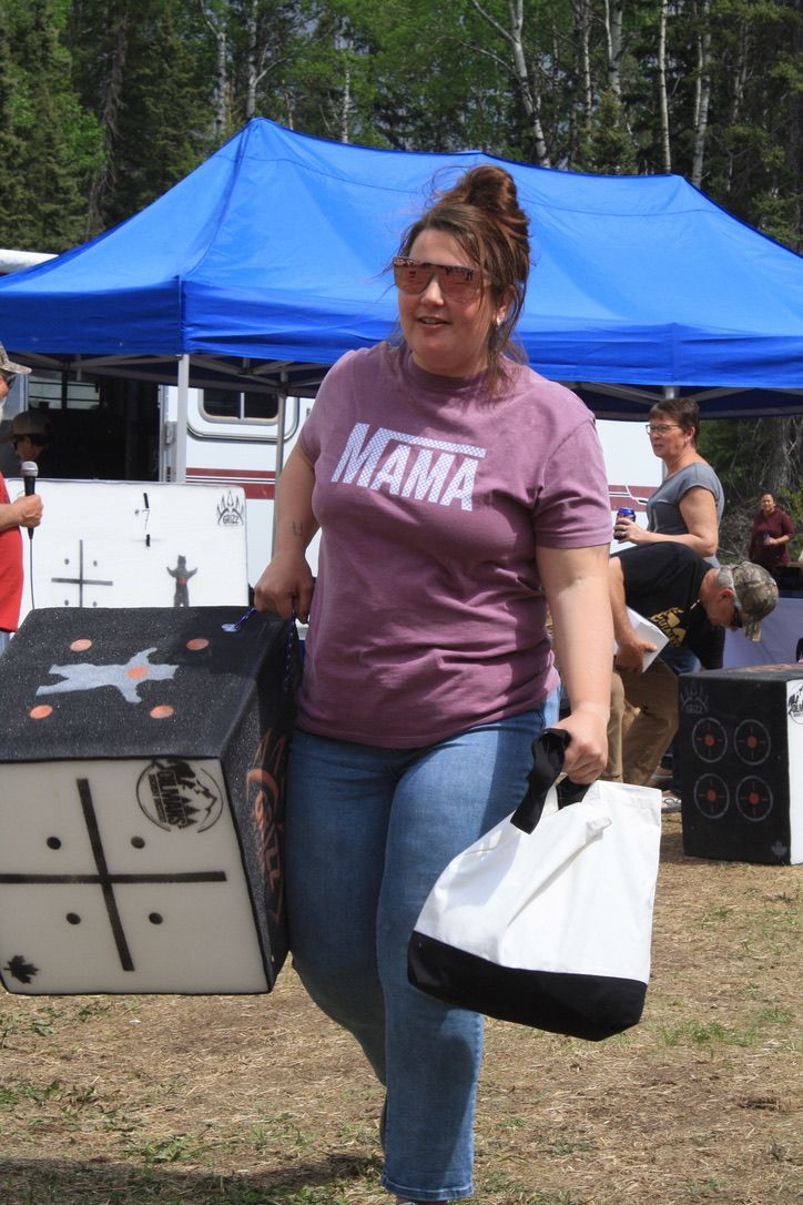 A woman wearing a mama shirt is carrying a bag and a box