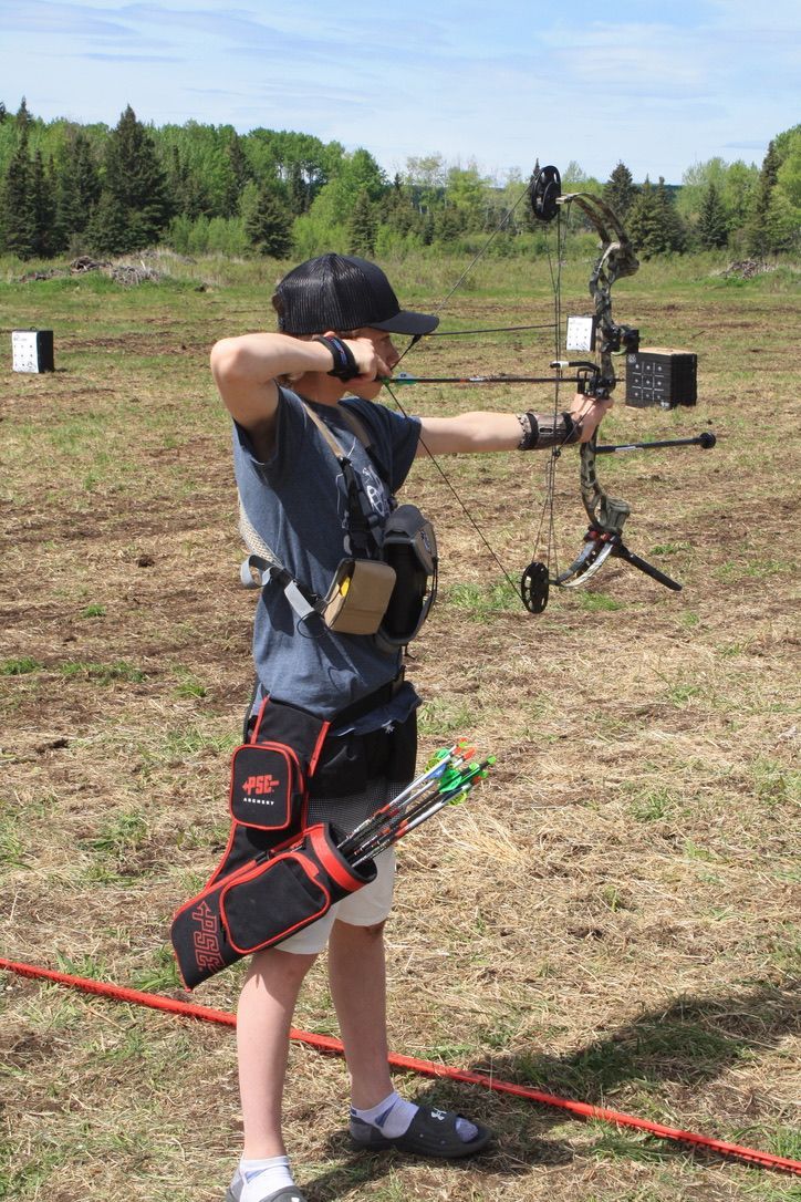 A young boy is practicing archery in a field.
