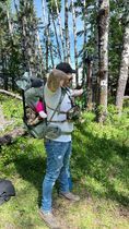 A man is carrying a baby in a backpack in the woods.