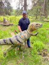 A man is standing next to a dinosaur statue in a field.